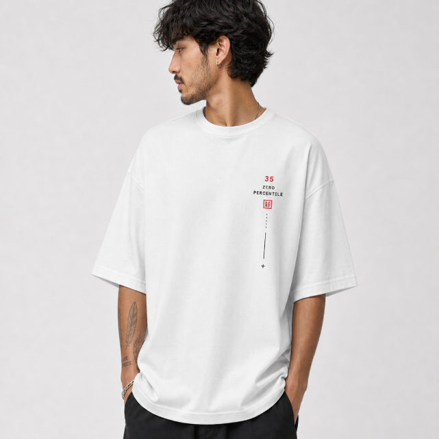 A man wearing an oversized white t-shirt with a small red and black graphic on the left chest, photographed against a light gray studio background.